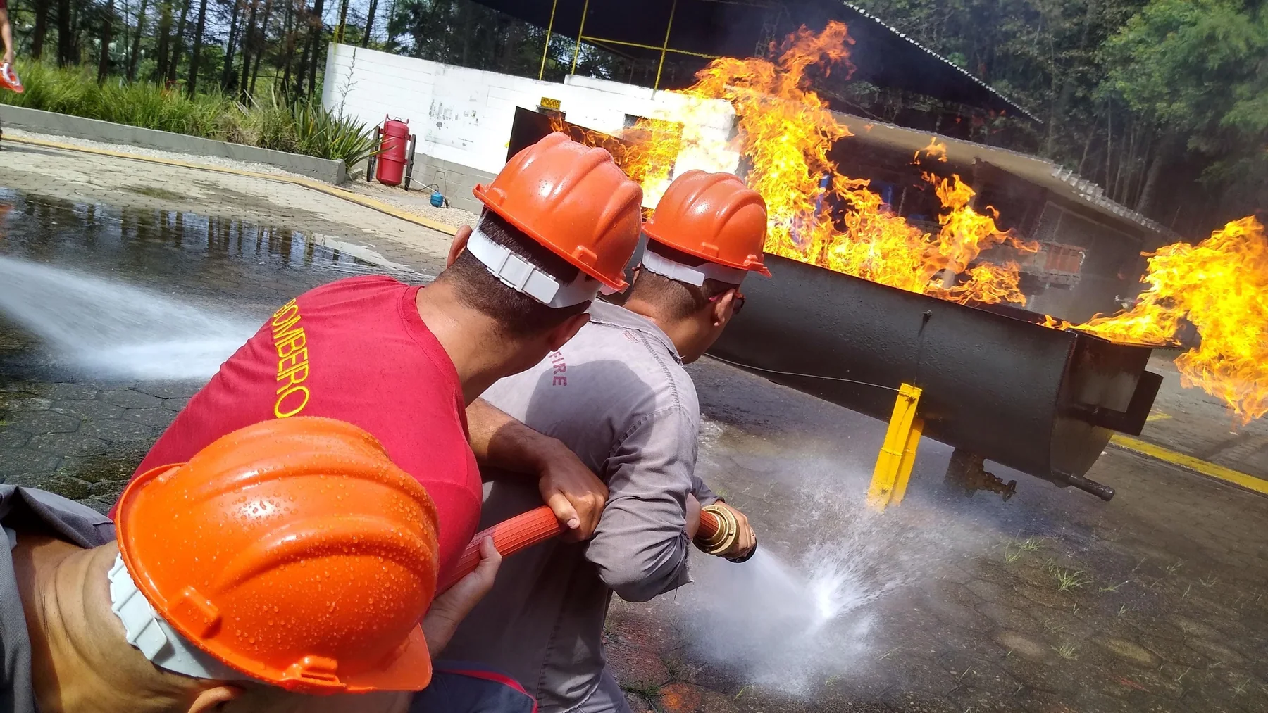 Equipe de brigada avançando com linha de mangueira sobre foco de incêndio, em treinamento conduzido pela Fox Team