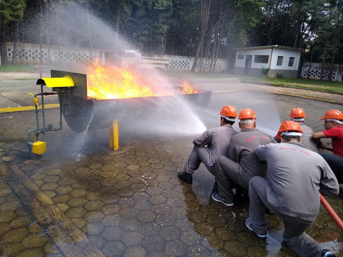 Turma atacando foco de incêndio em pista de treinamento com linha de mangueira