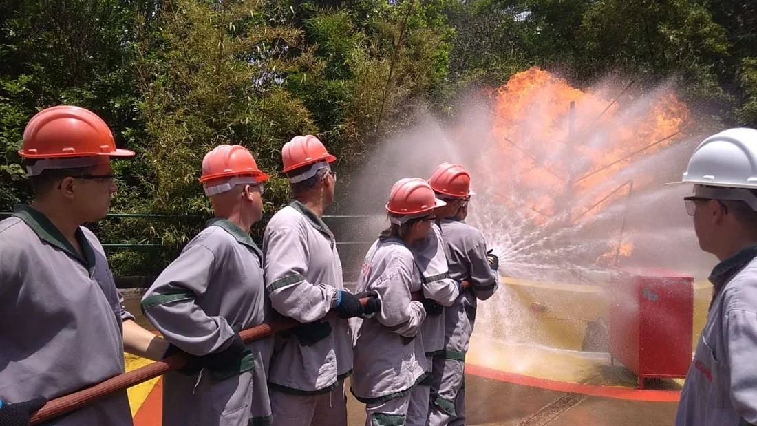 Brigadistas de capacete em linha, controlando a mangueira durante o combate